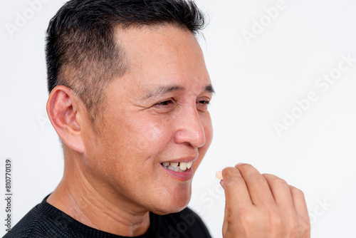 A confident Asian man in his forties smiles as he takes a chewable antacid tablet. Perfectly isolated on a white backdrop.