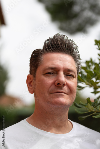 Portrait of an attractive 50 years old man with relaxed and happy attitude with gray hair with toupee, in a park one summer afternoon. Out of focus background. Concept of maturity