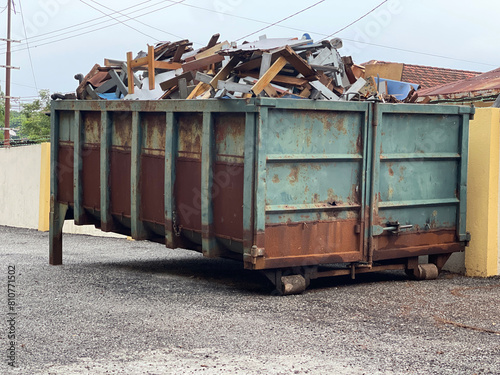 A dump truck bin  full of rubbish and materials placed nearby a building. photo