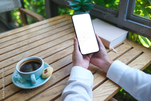 Mockup image of a woman holding mobile phone with blank desktop screen in cafe photo