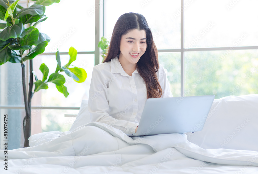 Asian beautiful woman girl in her bedroom smiling relaxed searching, playing social on her laptop on white bed in the morning after waking up at home, concept chat with someone online. Asian beautiful woman girl in her bedroom smiling relaxed searching, playing social on her laptop on white bed in the morning after waking up at home, concept chat with someone online.