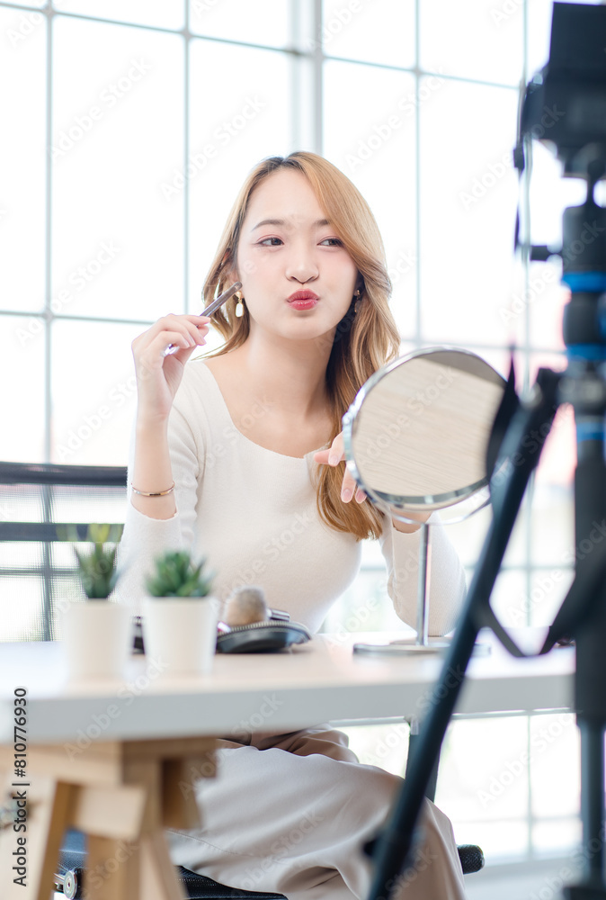 Asian beautiful smiling happy female influencers talk to camera sitting at home and doing her make-up. Young woman pretty long hair applying show lipstick on hand, makeover, at home. Asian beautiful smiling happy female influencers talk to camera sitting at home and doing her make-up. Young woman pretty long hair applying show lipstick on hand, makeover, at home.