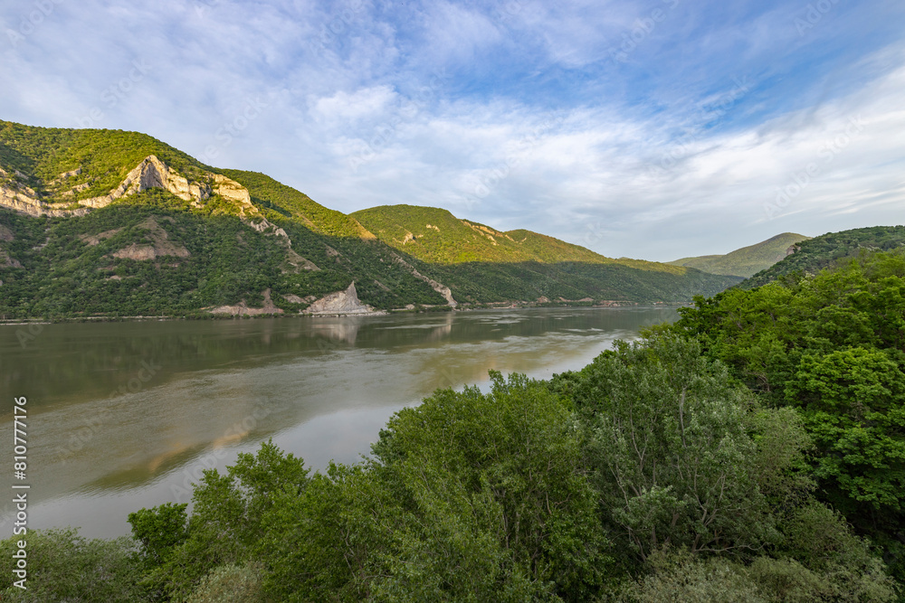  captures a serene river landscape, with calm water reflecting the greenery of the surrounding forest and the rugged cliffs on the opposite bank.