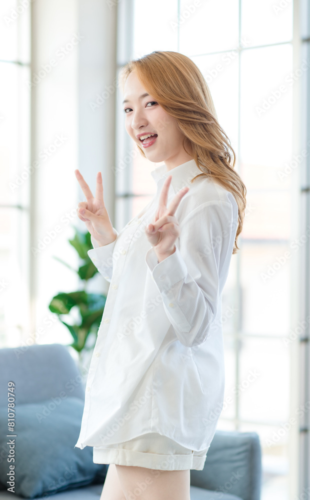 Asian beautiful female girls smile standing by the window, Cheerful young woman happy in the living room, feeling so relaxed at home weekend lifestyle in the morning. Healthcare concept Asian beautiful female girls smile standing by the window, Cheerful young woman happy in the living room, feeling so relaxed at home weekend lifestyle in the morning. Healthcare concept