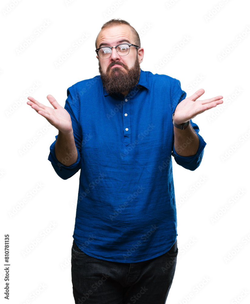 Young caucasian hipster man wearing glasses over isolated background clueless and confused expression with arms and hands raised. Doubt concept. Young caucasian hipster man wearing glasses over isolated background clueless and confused expression with arms and hands raised. Doubt concept.