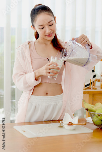 Sporty girl in fitness sport wear drinking healthy smoothie beverage that made for mix fruit and vegetable at kitchen. Beautiful happy smiling Asian woman trying to lose weight, slim and healthy.