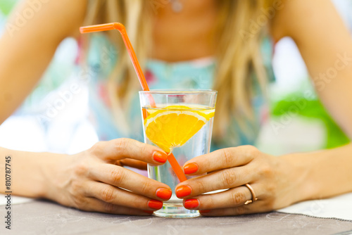 Close-up of a woman's hands holding a glass of water garnished with a fresh orange slice, symbolizing healthy lifestyle and hydration.