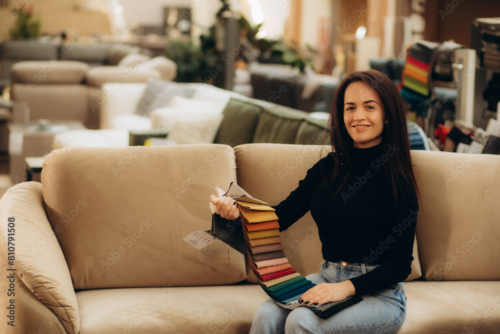 Obraz premium The woman chooses the fabric on the sofa. A young women looks at tissue samples. Selects the color of the sofa. Textile industry background. Tissue catalog.