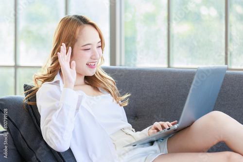 Happy young asian beautiful woman smiling sitting relaxed on cozy sofa in living room using laptop computer, shopping online, reading news, browsing internet at home, Girl using digital technology