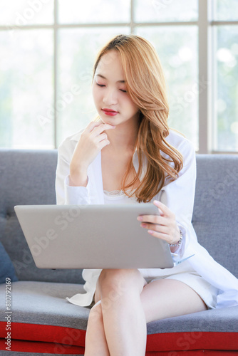 Happy young asian beautiful woman smiling sitting relaxed on cozy sofa in living room using laptop computer, shopping online, reading news, browsing internet at home, Girl using digital technology