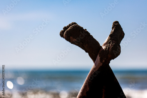 Quadro su tela Sandy legs crossed against a bright blue sea backdrop, relaxing on the beach