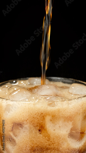 pouring cola into glass with ice, black background
