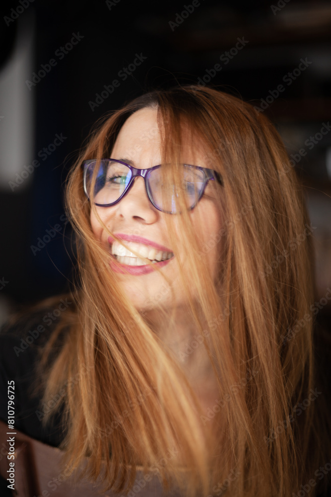 A joyful young woman with glasses and long blonde hair smiles broadly ...