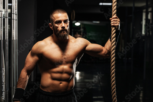 Focused muscular man in gym holding rope for fitness training