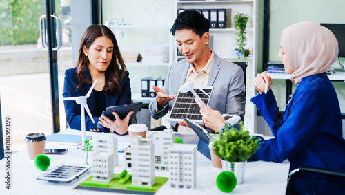 Trio of businesspeople, including a middle-aged Asian man and woman, strategize at their desk, prioritizing sustainability renewable energy adoption, waste reduction, and eco-friendly practices. photo