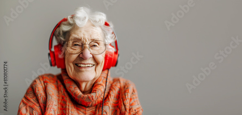 Smiling elderly woman with headphones, on gray background, copyspace