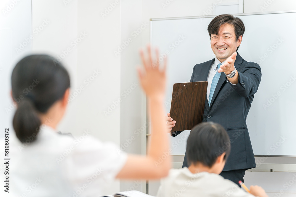 塾・学校の教室で小学生・中学生の子供に勉強を教える男性講師・教師
