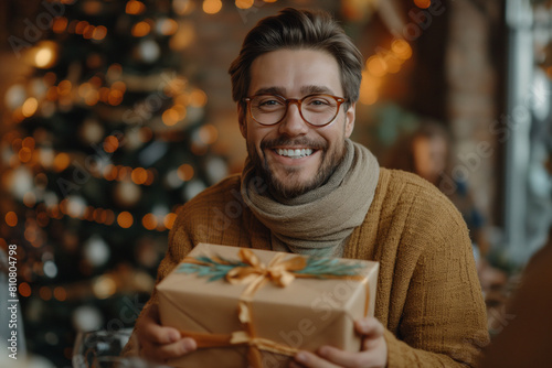 A young handsome man in a winter sweater against the background of a New Year's interior with a gift. New Year holidays concept. Christmas weekend and holidays. Boxing Day.