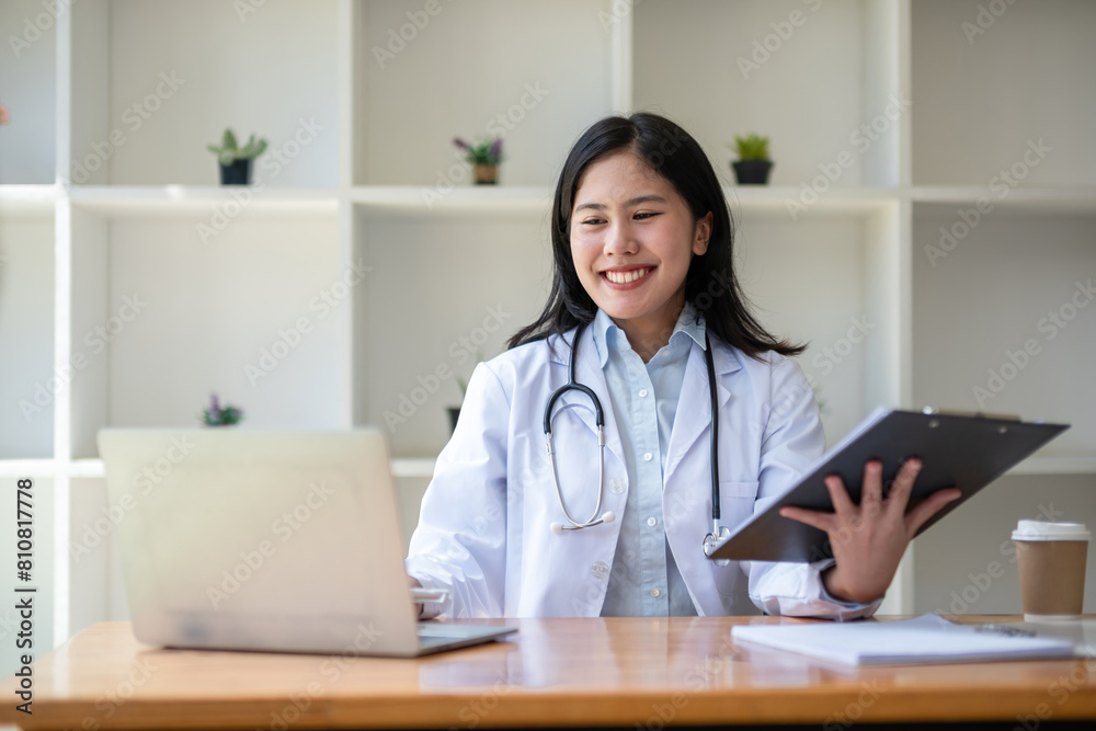 young asian lady doctor in white medical uniform with stethoscope using computer laptop talking video conference call with patient at desk in health clinic or hospital. young asian lady doctor in white medical uniform with stethoscope using computer laptop talking video conference call with patient at desk in health clinic or hospital.