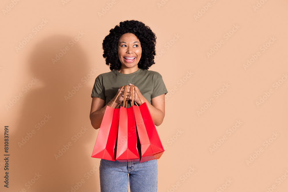 Photo of nice woman with afro hairstyle wear khaki t-shirt hold shopping bags look at sale empty space isolated on beige color background Photo of nice woman with afro hairstyle wear khaki t-shirt hold shopping bags look at sale empty space isolated on beige color background