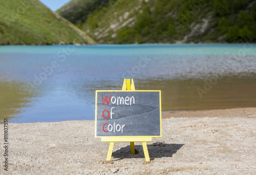 WOC women of color symbol. Concept words WOC women of color on beautiful yellow blackboard. Beautiful mountain lake background. Business WOC women of color social issues concept. Copy space.