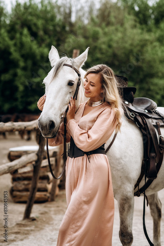 Beautiful blonde girl in a long dress with a white horse