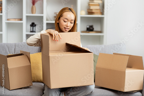 Young Woman Unpacking Boxes In New Home, Exuding Happiness And New Beginnings, A Relatable Lifestyle Scene Capturing Moving Day Excitement In A Modern Living Room. © puhhha