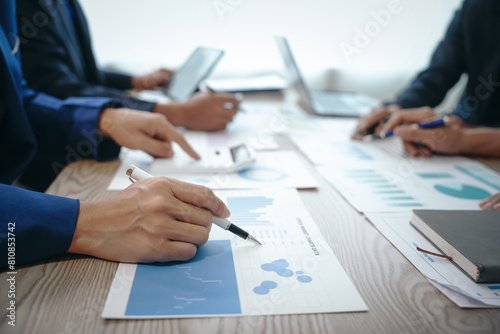A professional business team meeting in formal suits, working at desks with financial papers, calculators, and laptops. Close-up of hands. Discussion on revenue, brand, sales, agenda, capital