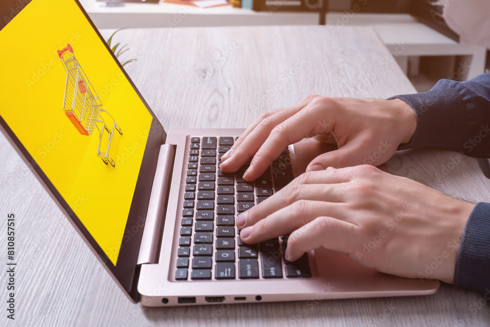 Fototapeta premium Hands typing on laptop keyboard with shopping cart on display. Concept image of online shopping. Modern digital retail experience