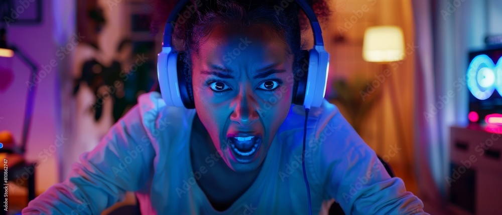 In this picture, a pretty and excited black gamer girl wears headphones while playing online video game. The room and computer have colorful neon led lights. In this picture, a pretty and excited black gamer girl wears headphones while playing online video game. The room and computer have colorful neon led lights.