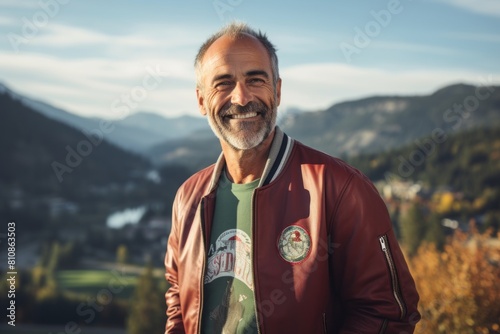 Portrait of a happy man in his 50s sporting a stylish varsity jacket while standing against panoramic mountain vista