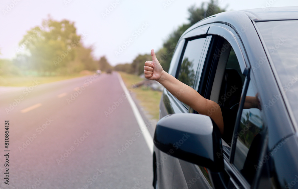 Woman inside car on the road trip with thumb up gesture out of the window with copy space for banner. Front view Woman inside car on the road trip with thumb up gesture out of the window with copy space for banner. Front view
