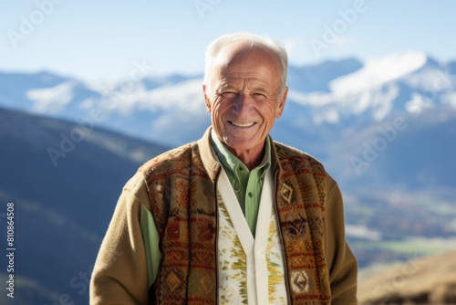 Portrait of a grinning man in his 60s wearing a chic cardigan in panoramic mountain vista