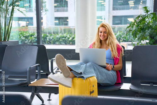 Young beautiful woman smiling, looking at laptop and chatting. Modern light airport before flight