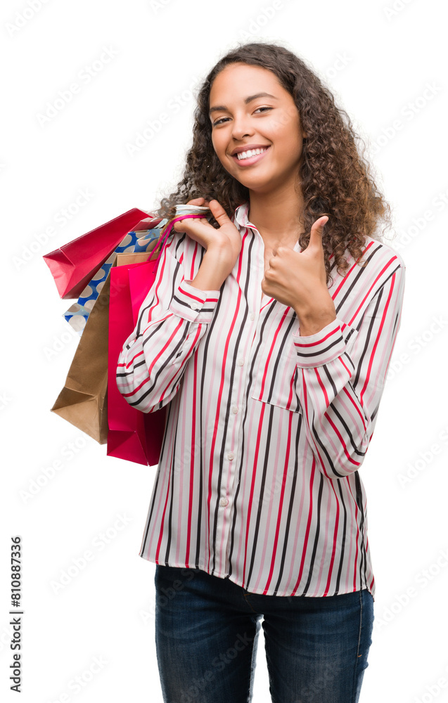 Young hispanic woman holding shopping bags happy with big smile doing ok sign, thumb up with fingers, excellent sign Young hispanic woman holding shopping bags happy with big smile doing ok sign, thumb up with fingers, excellent sign