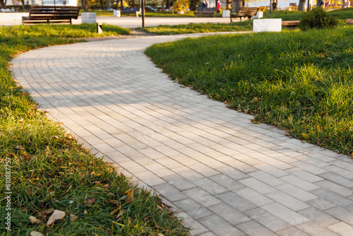 The curved path in the park is paved with gray concrete paving slabs. Selective focus.