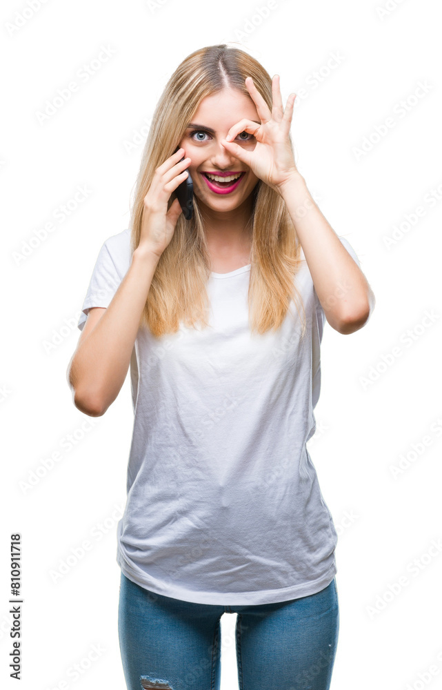 Young beautiful blonde woman talking using smartphone over isolated background with happy face smiling doing ok sign with hand on eye looking through fingers Young beautiful blonde woman talking using smartphone over isolated background with happy face smiling doing ok sign with hand on eye looking through fingers