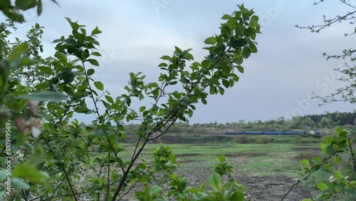 Fast train going through the field. View of railroad in Ukraine. Railway landscape on blue sky background.