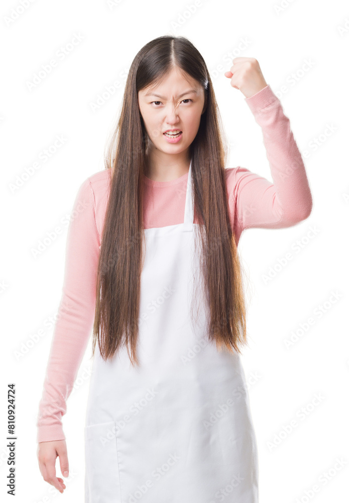 Young Chinese shop owner woman over isolated background wearing white apron annoyed and frustrated shouting with anger, crazy and yelling with raised hand, anger concept