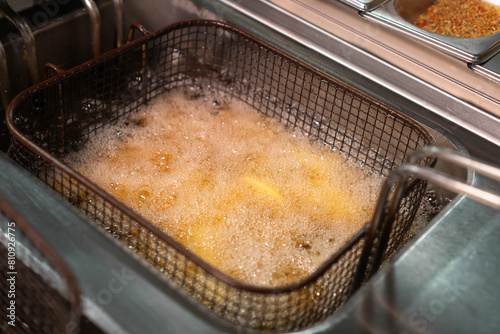 Close-up of potatoes in large slices is cooked in a deep fryer. Potatoes are rustic fried in oil in a deep fryer in the kitchen.