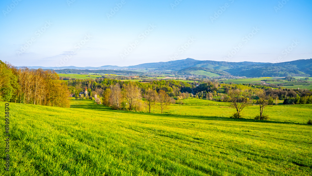 A breathtaking view of the Jested Ridge horizon, captured from a lush green field under a clear blue sky. The serene atmosphere suggests early morning or late afternoon. Located in Czech Republic