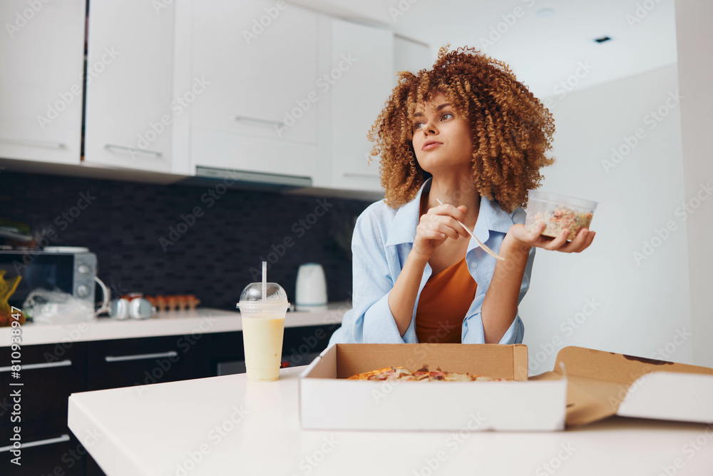 Curly haired woman enjoying pizza while standing in kitchen holding pizza box Curly haired woman enjoying pizza while standing in kitchen holding pizza box