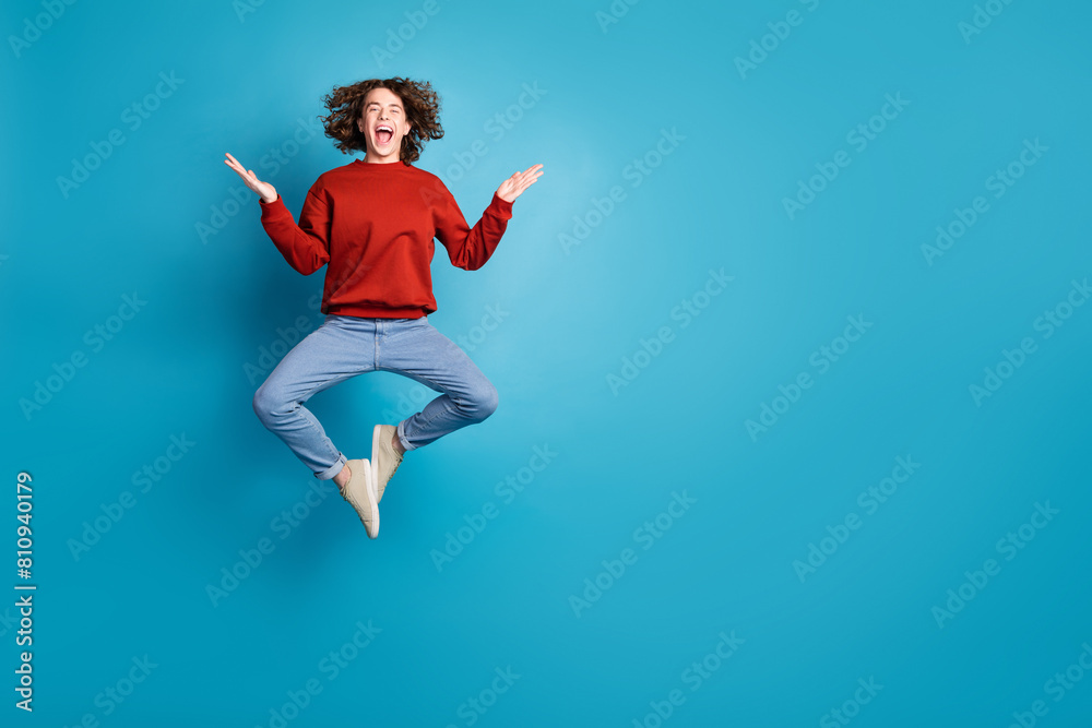 Full length photo of funky impressed guy dressed red pullover jumping high emtpy space isolated blue color background Full length photo of funky impressed guy dressed red pullover jumping high emtpy space isolated blue color background