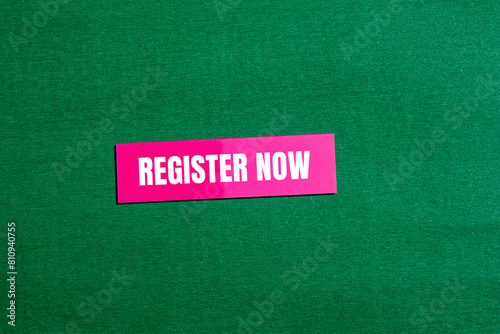 Register now words written on pink paper sticker with green background. Conceptual register now symbol. Copy space.