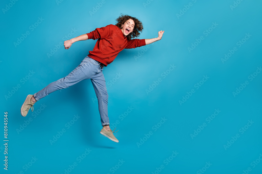 Full length photo of funky cool guy dressed red pullover jumping high hurrying emtpy space isolated blue color background