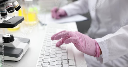 Scientist chemist in gloves typing on keyboard and writing down information on paper closeup 4k movie slow motion. Development of chemical innovations concept