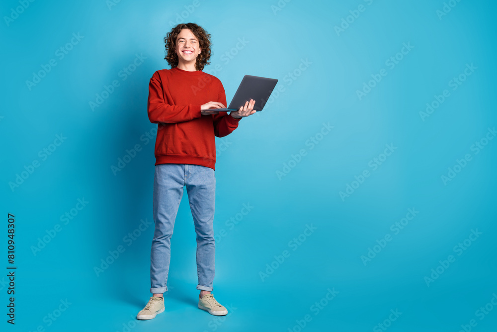 Full length photo of cheerful positive guy dressed pullover typing apple samsung gadget empty space isolated blue color background Full length photo of cheerful positive guy dressed pullover typing apple samsung gadget empty space isolated blue color background