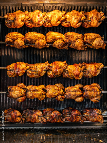 Grilled chickens on a spit, background of steamy rotisserie machine. Popular food