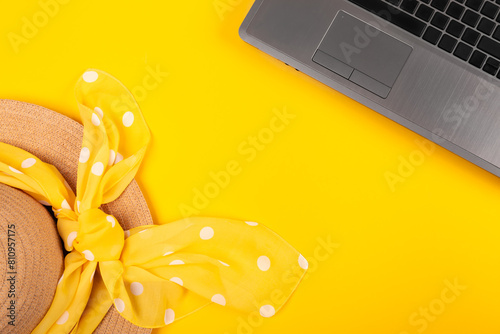 Laptop and straw hat with kerchief in white polka dots on yellow background. Work at holiday. Concept of travelling on summer vacation. Business trip to the south. Freelancer's job. Working weekend