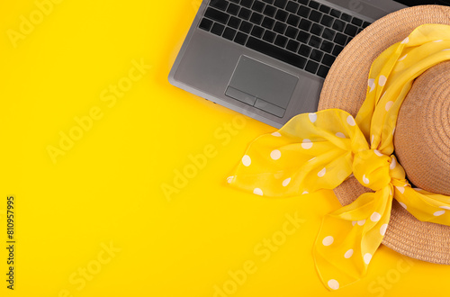 Laptop and straw hat with kerchief in white polka dots on yellow background. Work at holiday. Concept of travelling on summer vacation. Business trip to the south. Freelancer's job. Working weekend